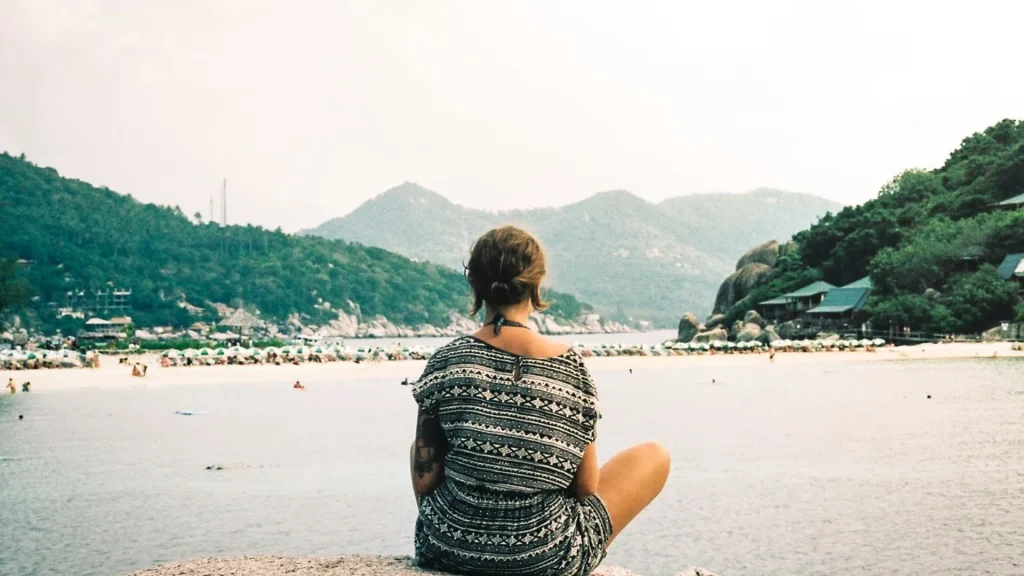 Couples travel psychology: a traveler taking quiet time alone on a rock, gazing over a calm tropical bay