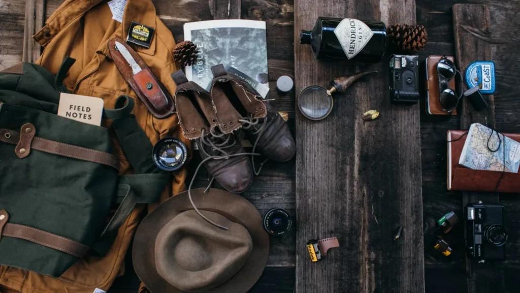 Flat lay of travel essentials including backpack, boots, hat and field notes