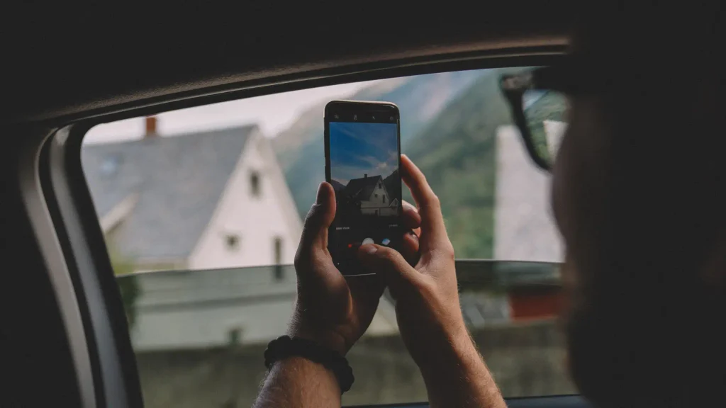 Traveler taking a photo of a mountain village on a phone through a car window Travel Journaling