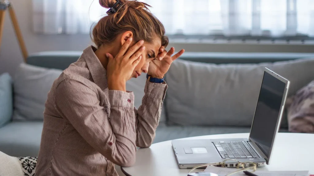 Stressed woman pressing her temples at a laptop, feeling overwhelmed while planning a trip, use AI trip planner